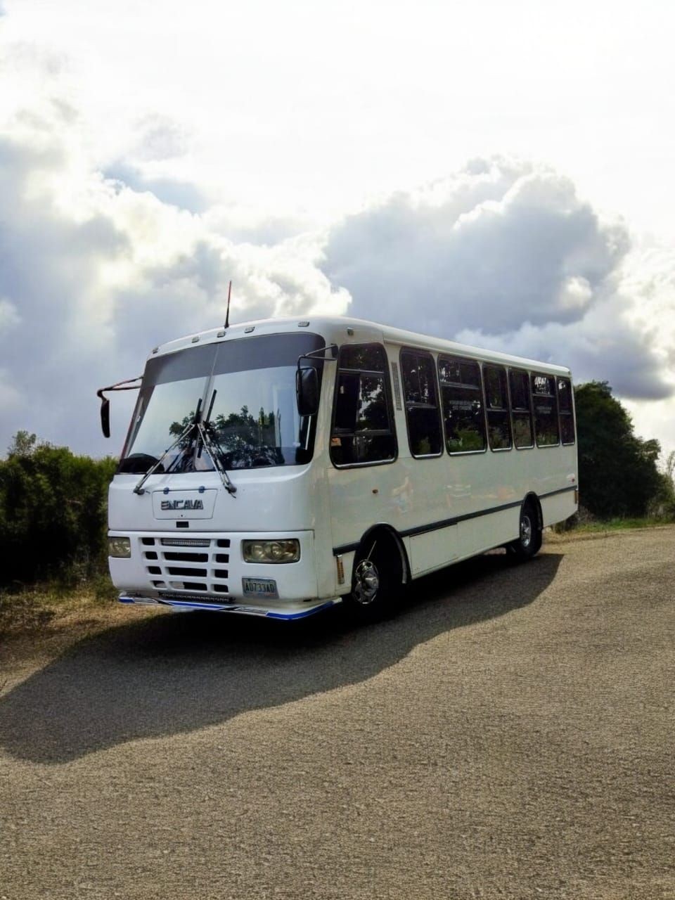 White passenger bus parked on a rural road under a cloudy sky.
