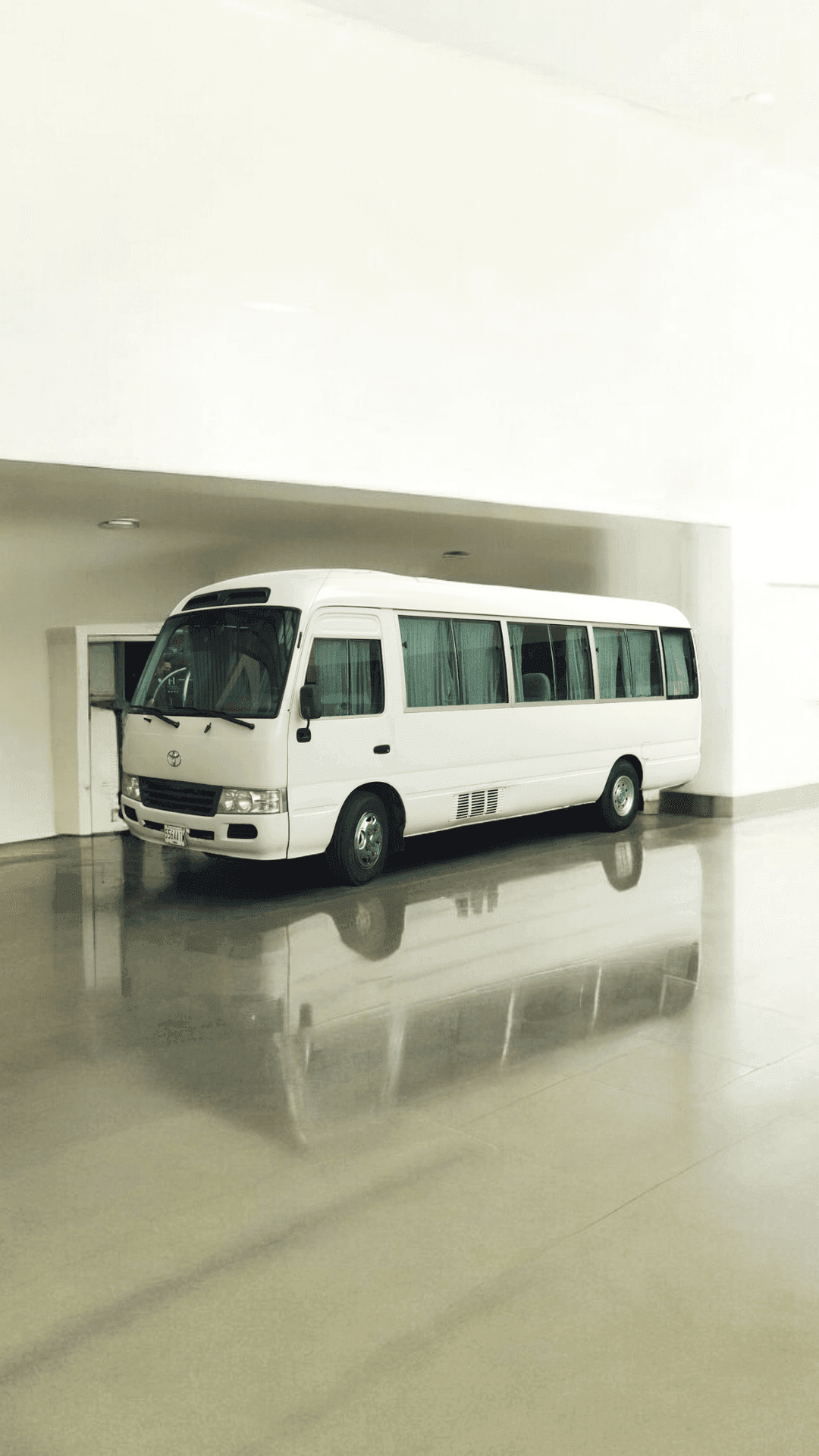 White minibus parked indoors with a shiny floor reflecting the vehicle.