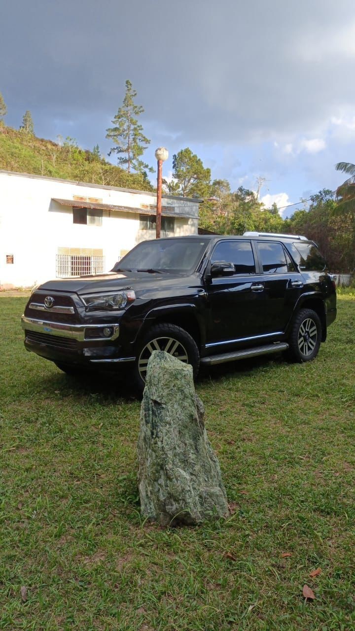 Black SUV parked on grass with a large rock in the foreground and white building in the background.